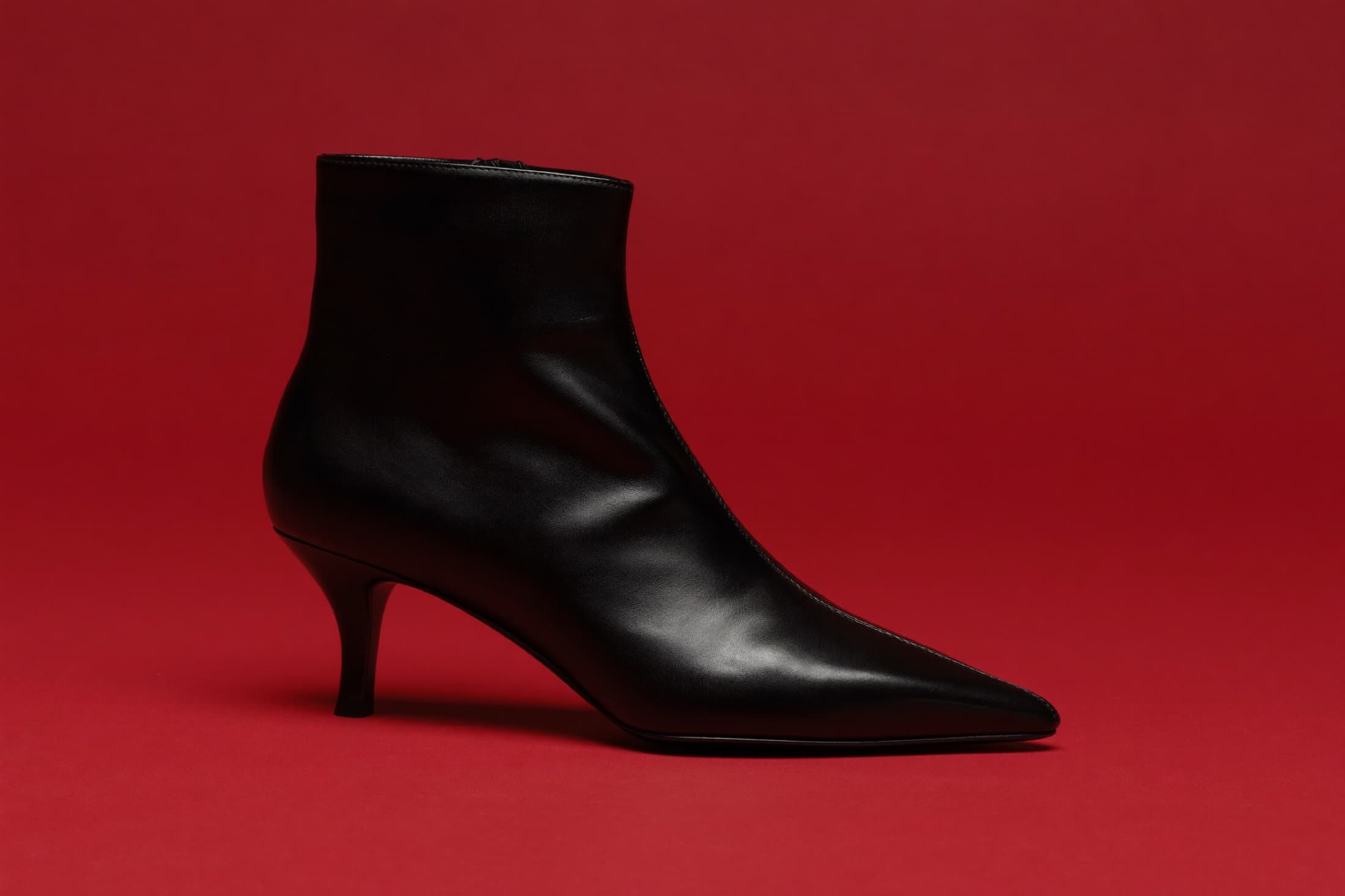 A sleek black Szya leather ankle boot on a bold cadmium-red ground